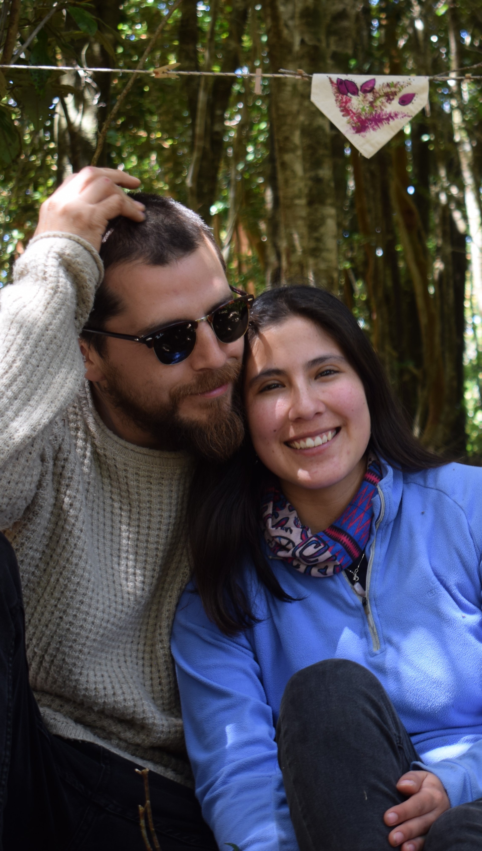Paz y David, fundadores de Ko Glamping, abrazados y sonrientes en bosque nativo.