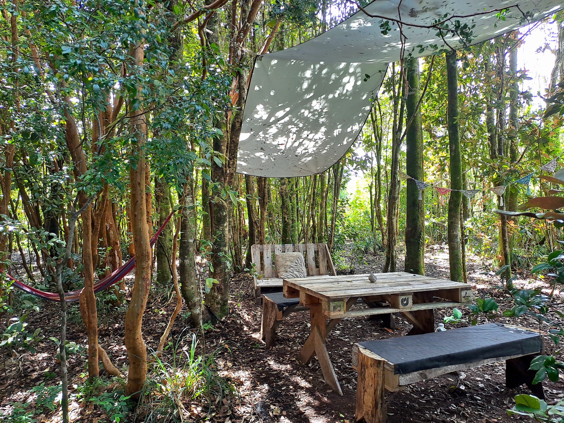 Sitio de camping Lafken en Ko Glamping, vacío, con mesa, asientos y hamaca, rodeado de bosque.