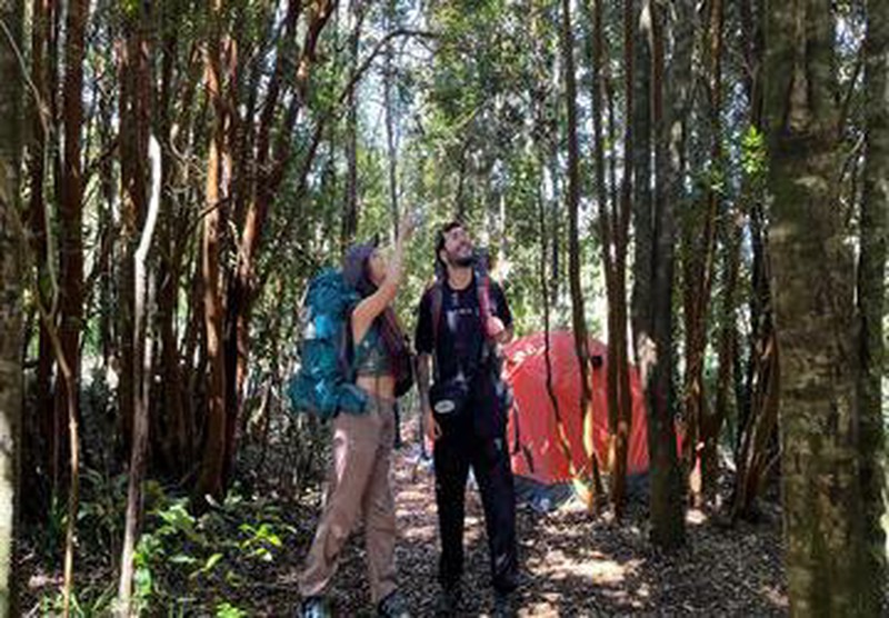 Campistas con mochilas en bosque de Ko Glamping, con carpa al fondo.