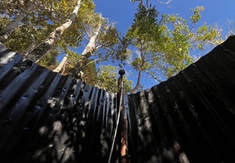 Ducha caliente al aire libre en Ko Glamping, rodeada de árboles y cielo descubierto.