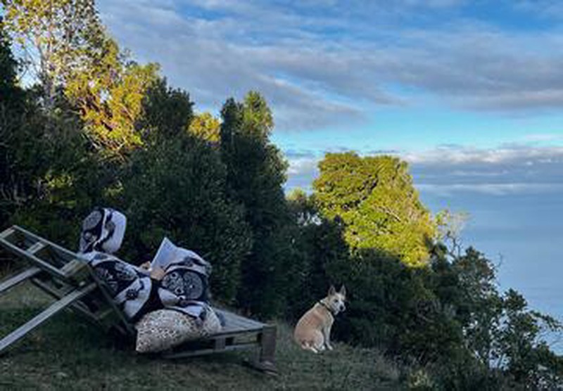 Hombre con poncho leyendo en asiento rústico frente al mar en Ko Glamping.